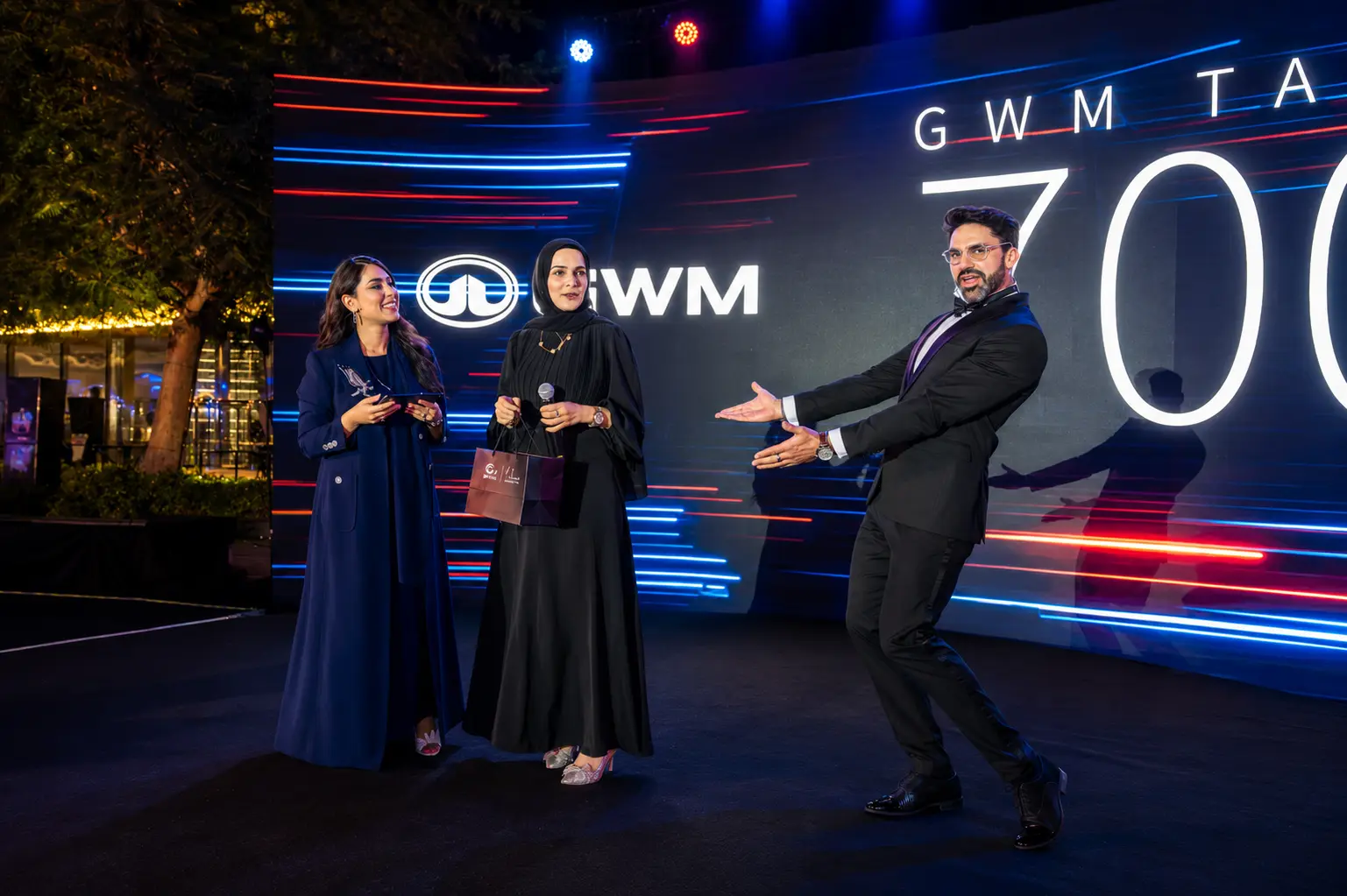 Professional MC engaging guests on stage during a GWM TANK 700 launch event in Dubai, with a large branded LED screen in the background.