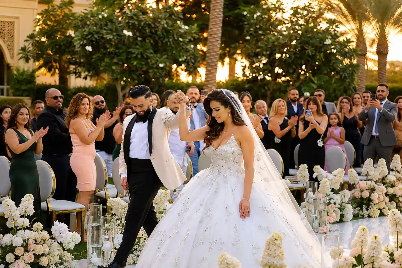 Bride and groom celebrating after their outdoor Dubai wedding ceremony, surrounded by applauding guests, palm trees and elegant white floral decor.